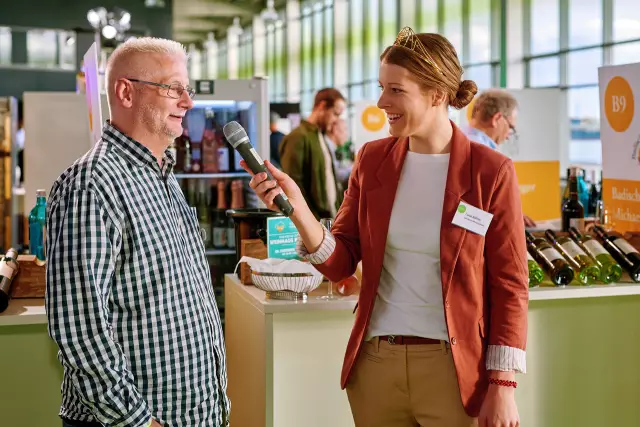 Luise Böhme, Deutsche Weinprinzessin 2022/2023 interviewt einen Gast der WeinTOUR-Messe in Hamburg. Die Önologin aus Laucha / OT Kirchscheidungen (Saale-Unstrut) studiert an der Hochschule Geisenheim und vertritt im Amtsjahr - wie ihre Kolleginnen - alle Weinerzeuger Deutschlands. Als ehemalige Leistungssportlerin behält Luise auch in stressigen Situationen immer einen kühlen Kopf.